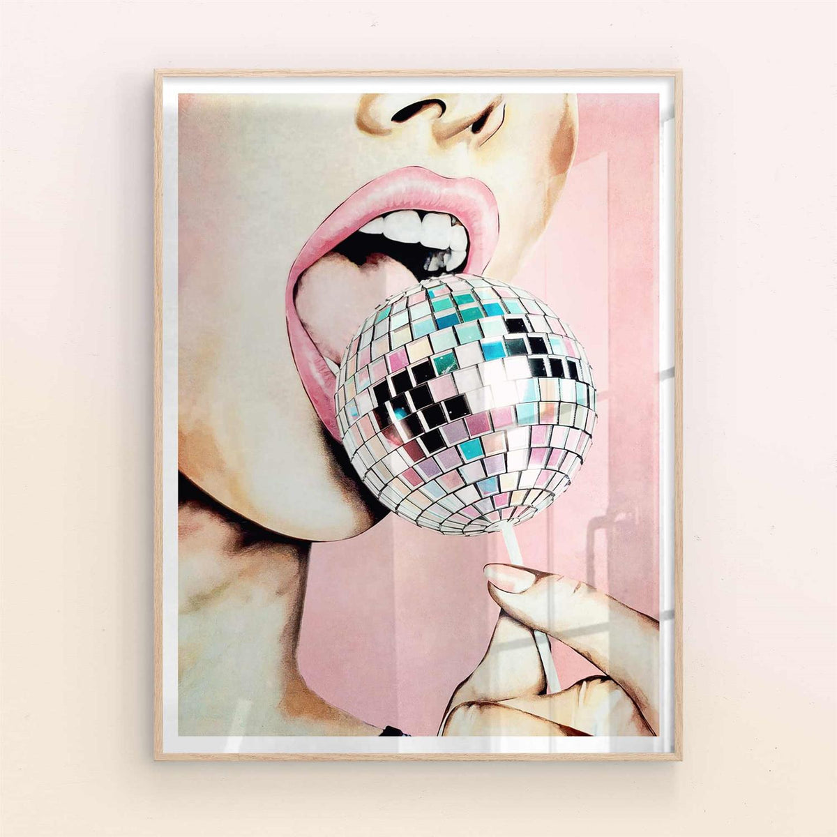 Framed artwork of a person's mouth holding a disco ball against a light pink background with natural/oak frame
