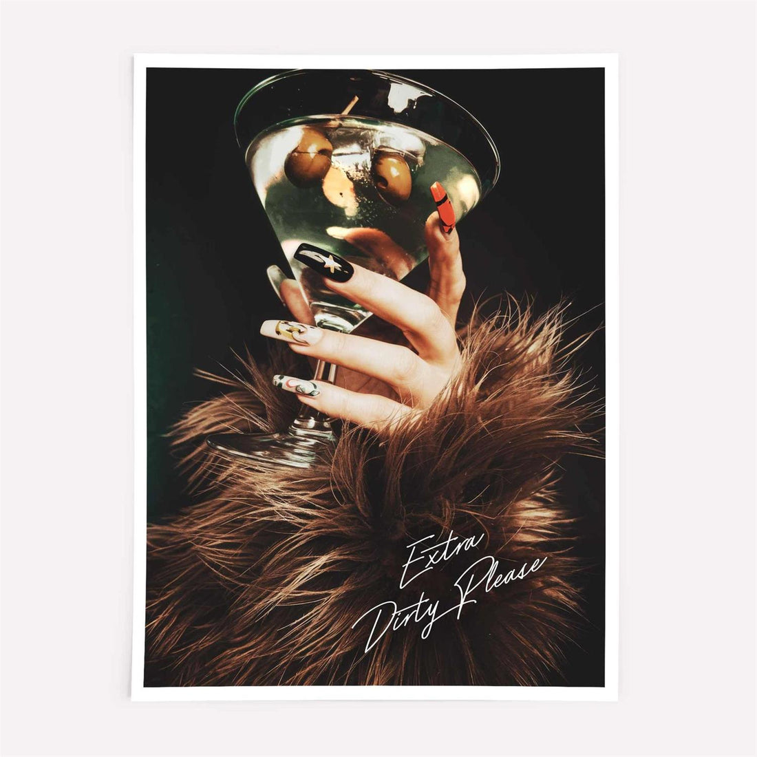 Framed artwork of a hand holding a cocktail with 'Extra Dirty Please' text on a beige wall with black frame