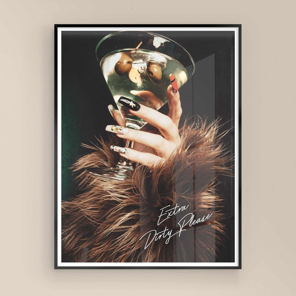 Framed artwork of a hand holding a cocktail with 'Extra Dirty Please' text on a beige wall with black frame