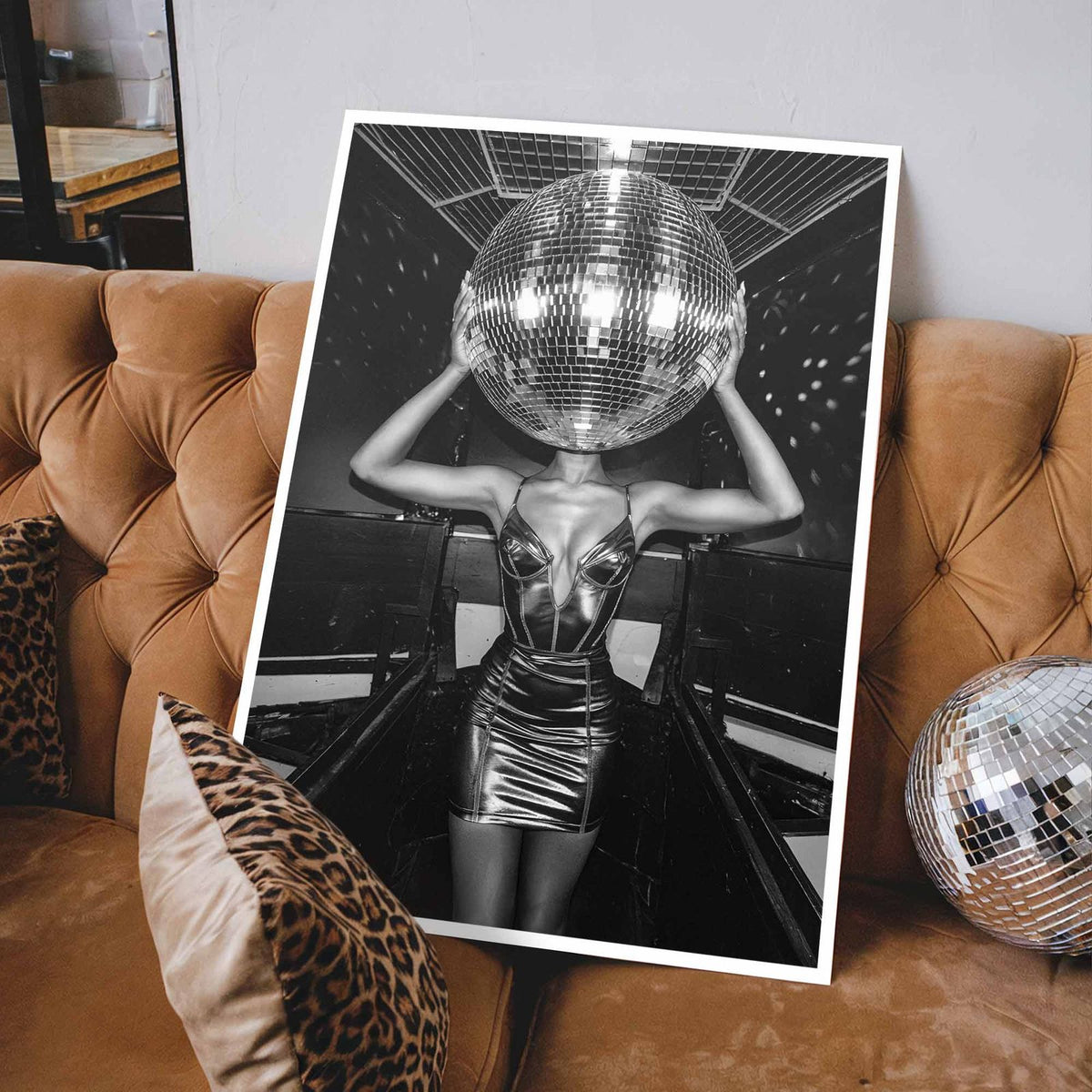 Poster of a person with a disco ball for a head on a brown sofa with leopard print pillows - white frame