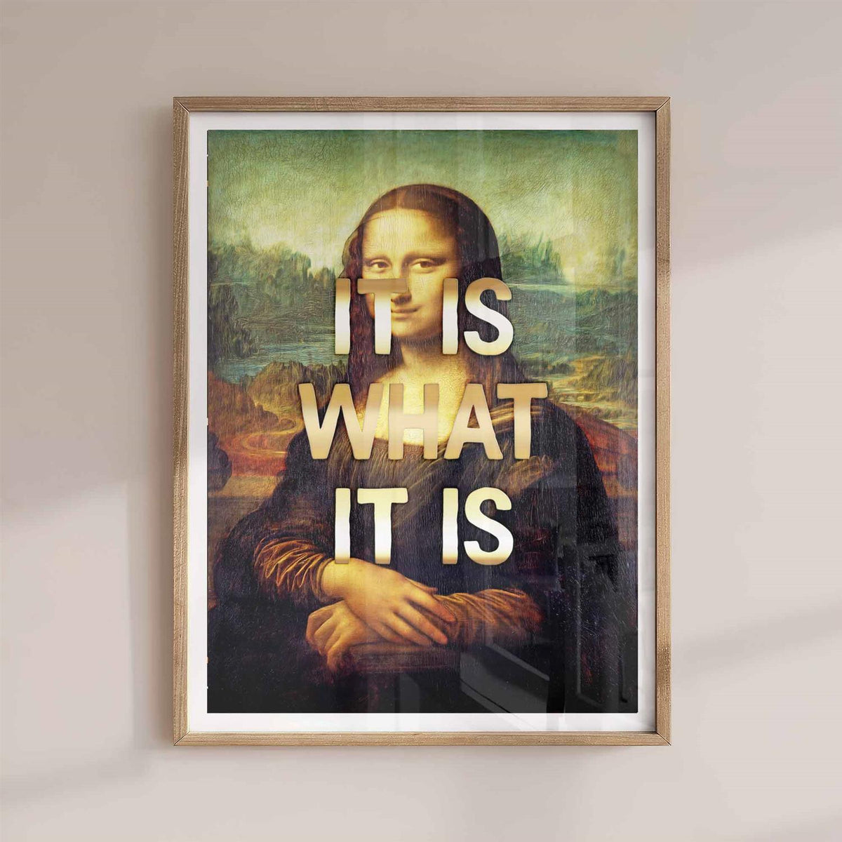 Framed artwork of Mona Lisa with 'It is what it is' text overlay on a plain wall with a natural or oak frame