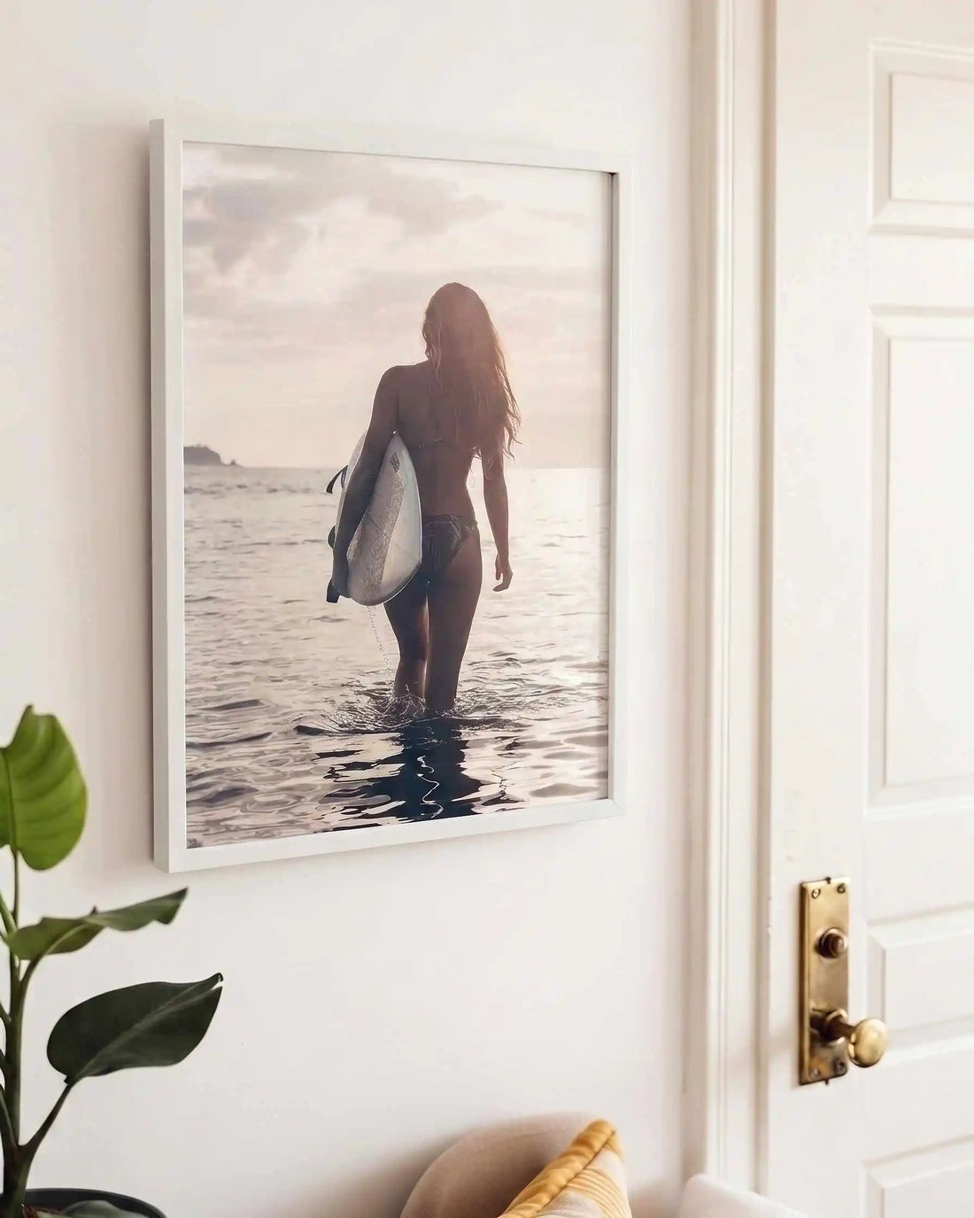 Surfer girl walking into the ocean at golden hour carrying a surfboard during sunset, creating a peaceful coastal photography framed wall art print.
